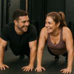 Man and woman smiling at each other while doing exercise, push-ups in a gym.