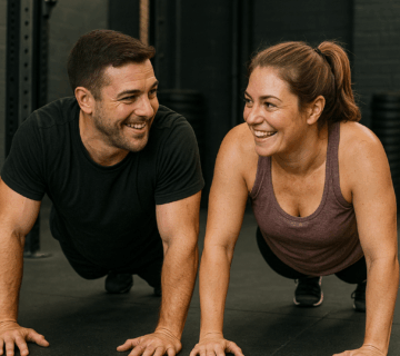 Man and woman smiling at each other while doing exercise, push-ups in a gym.
