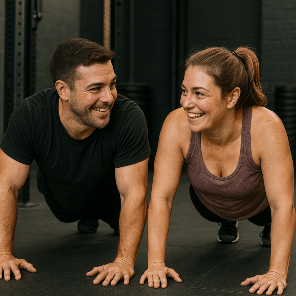 Man and woman smiling at each other while doing exercise, push-ups in a gym.